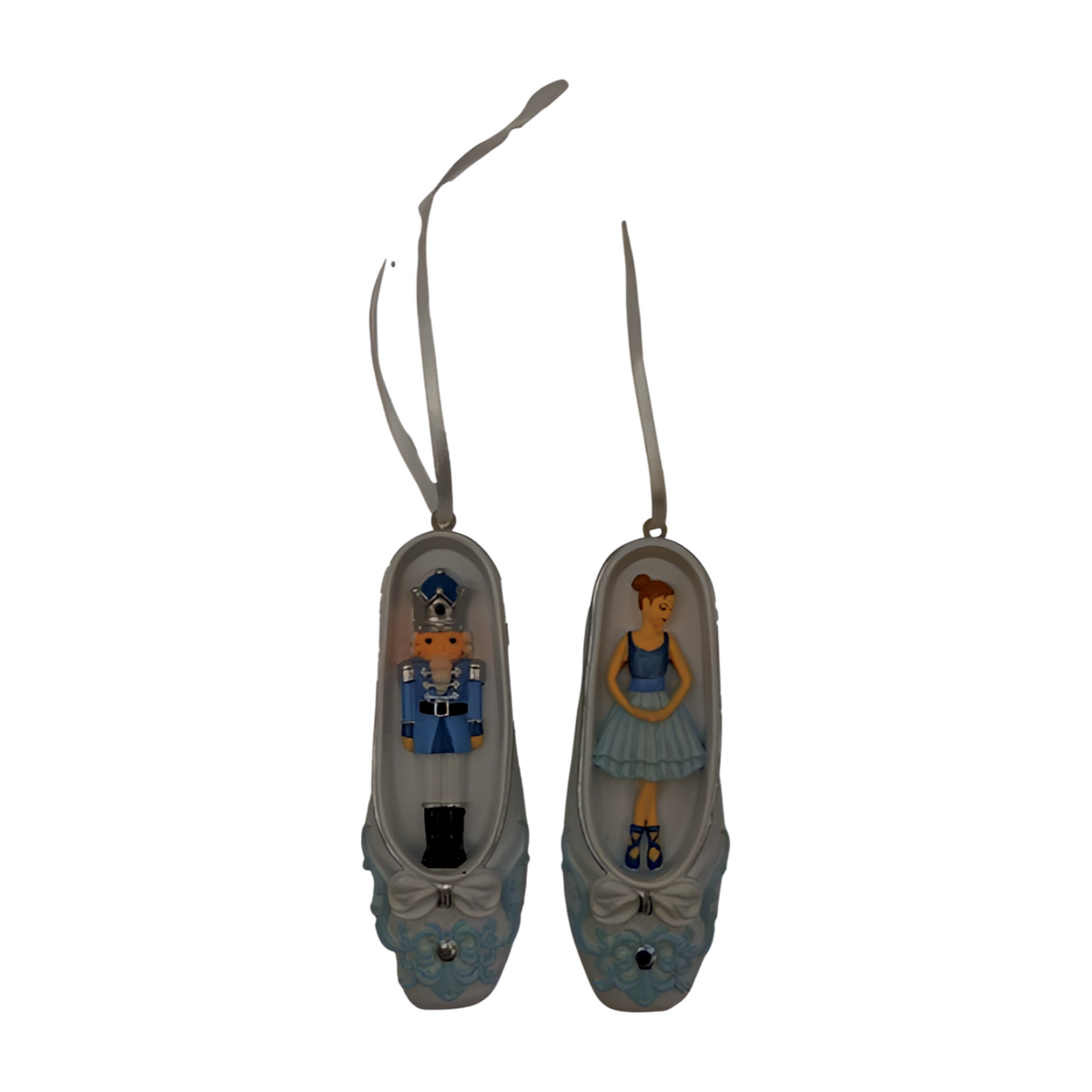 Two blue and white ballet slipper Christmas ornaments, one with a nutcracker figure and one with a ballerina figure, ribbon hangers.