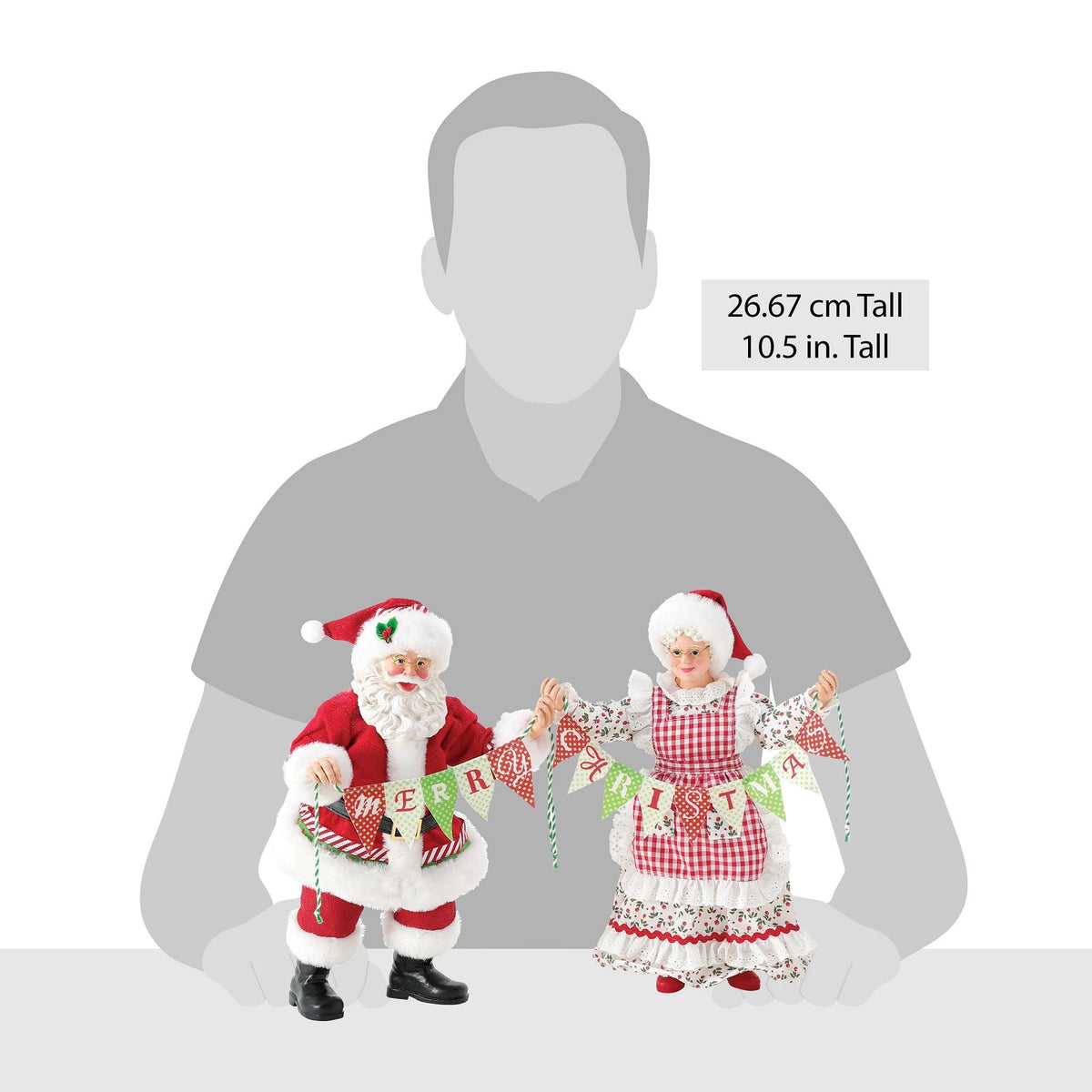 Santa and Mrs. Claus figurines holding a "Merry Christmas" banner shown against a human silhouette for scale, 26.67 cm / 10.5 inches tall
