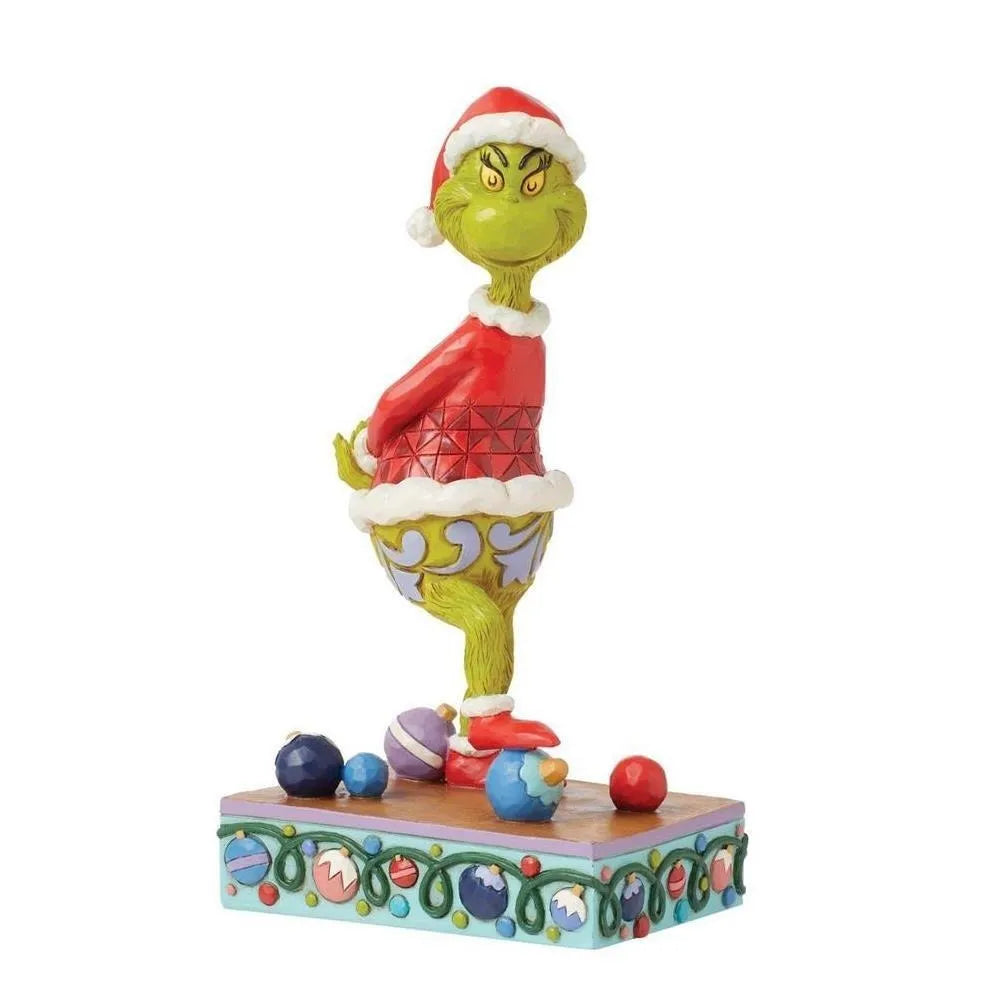 Three-quarter rear view of a Grinch Santa figurine with a scowling expression, one foot on a bauble, on an ornament-detailed base