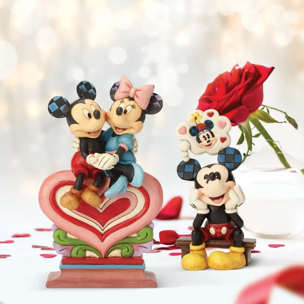 Mickey and Minnie Mouse heart figurine displayed with a second Mickey daydreaming figurine, red rose, and scattered heart confetti