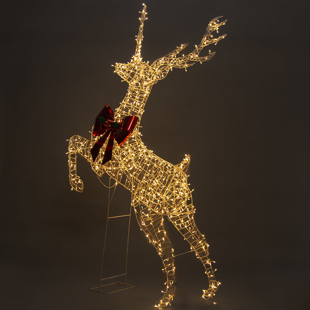 Silver wire leaping reindeer LED light figure with red bow, side view lit with warm white lights