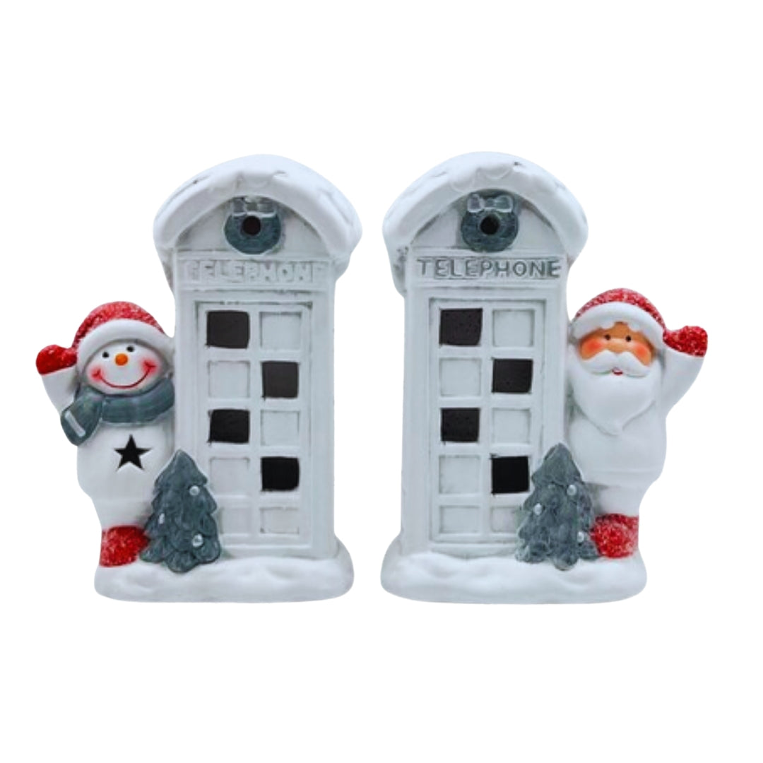 Two light-up snowy white telephone box decorations, one with a snowman and one with Santa, beside small trees
