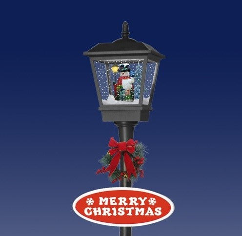 Close-up of black musical lamp post lantern with snowman snow effect scene and festive wreath detail
