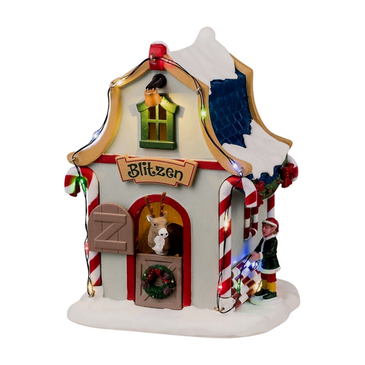 Angled front view of Blitzen's reindeer stable village building with Blitzen sign, reindeer in arched doorway, and elf figurine