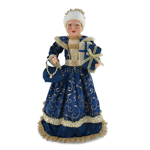 Mrs Claus wearing a blue dress with gold accents, holding two presents in one hand and a blue handbag in the other