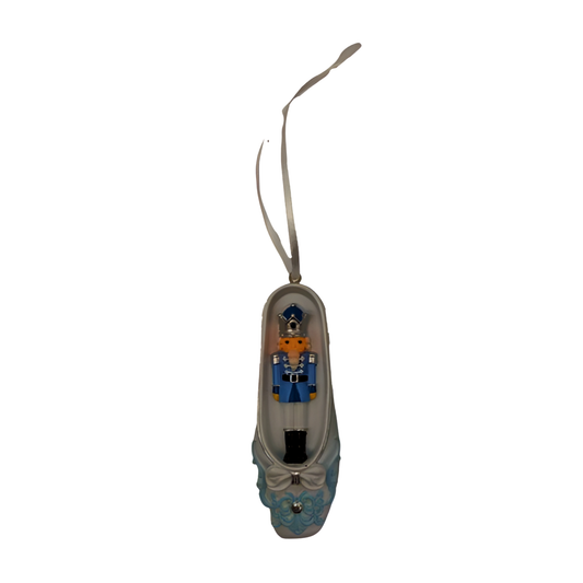 White and blue ballet slipper Christmas ornament with miniature nutcracker soldier figure inside, bow and floral detail, ribbon hanger.