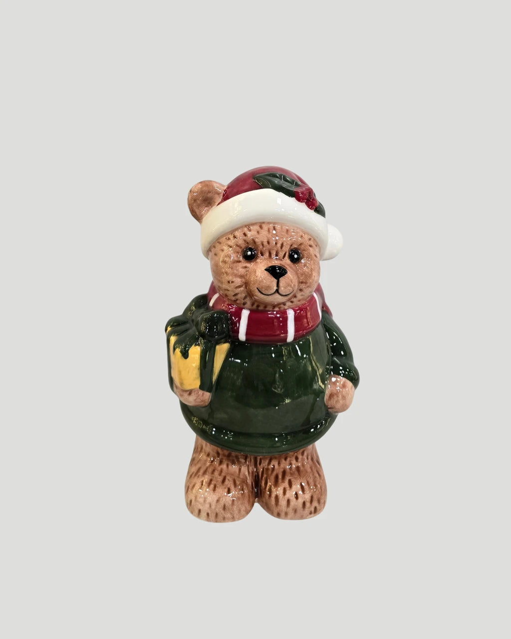 Ceramic teddy bear figure in santa hat holding a wrapped gift on plain background