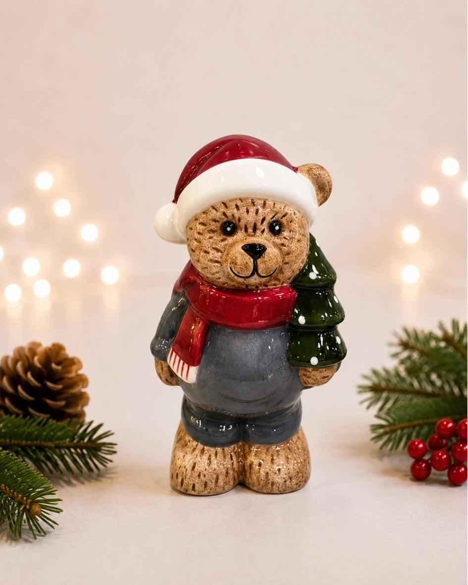 Ceramic teddy bear figure in santa hat holding a Christmas tree, styled with pinecone and berries