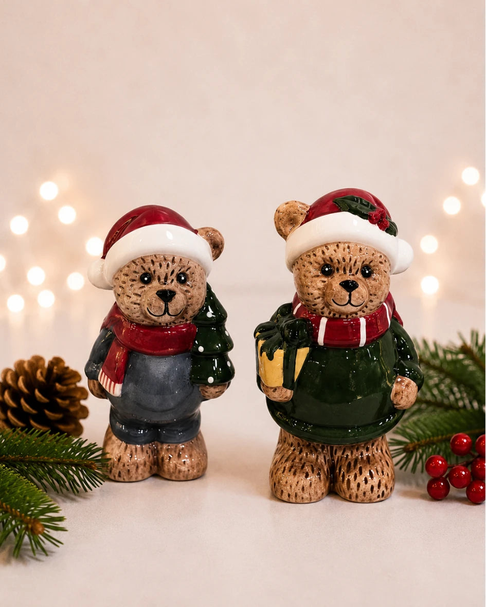 Ceramic teddy bear figures in santa hats, one holding a tree, one holding a gift, styled together
