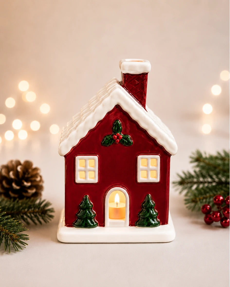 Lit ceramic red house tea light holder styled with Christmas tree and wrapped gift