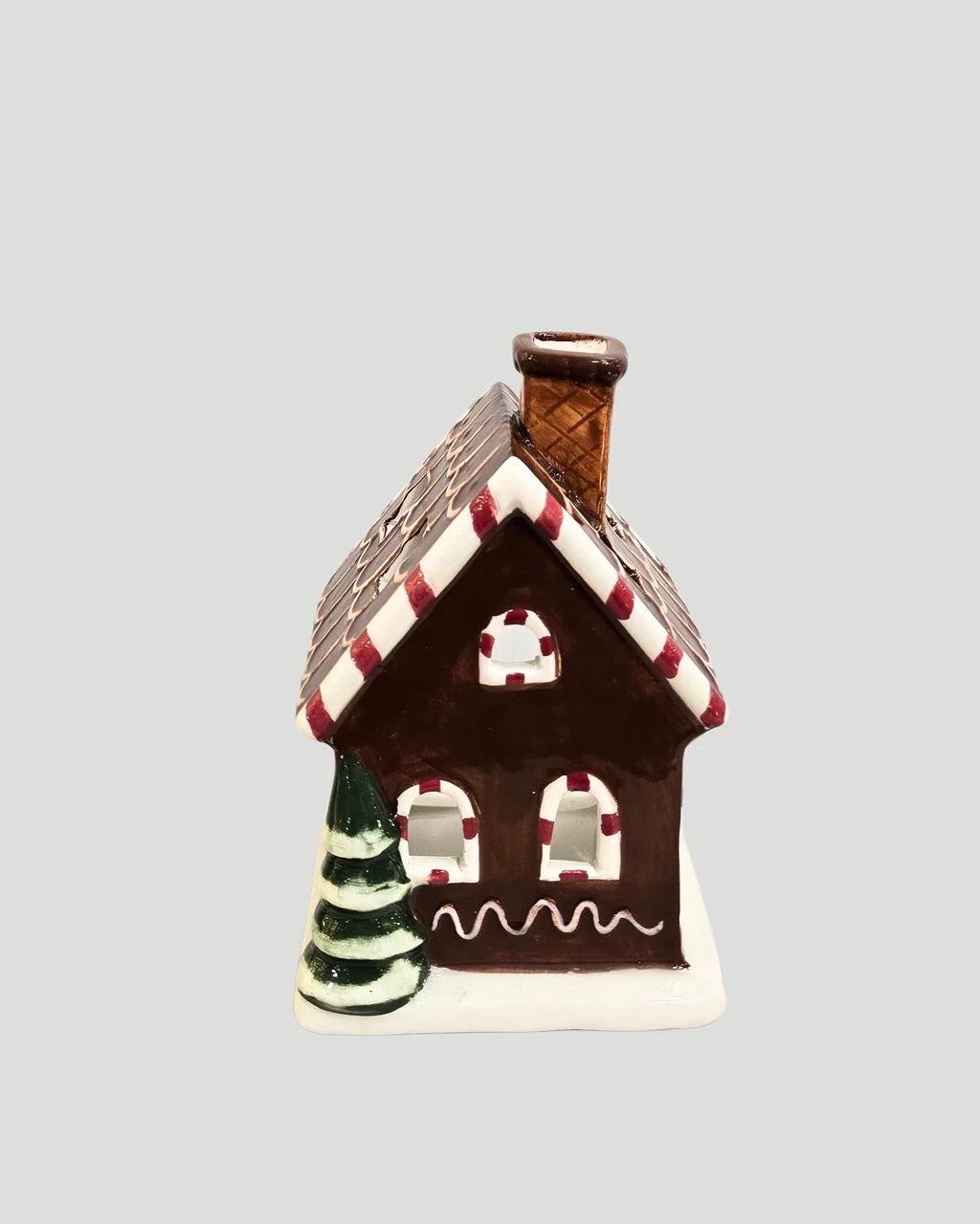 Ceramic gingerbread house tea light holder with candy-striped roof on plain background