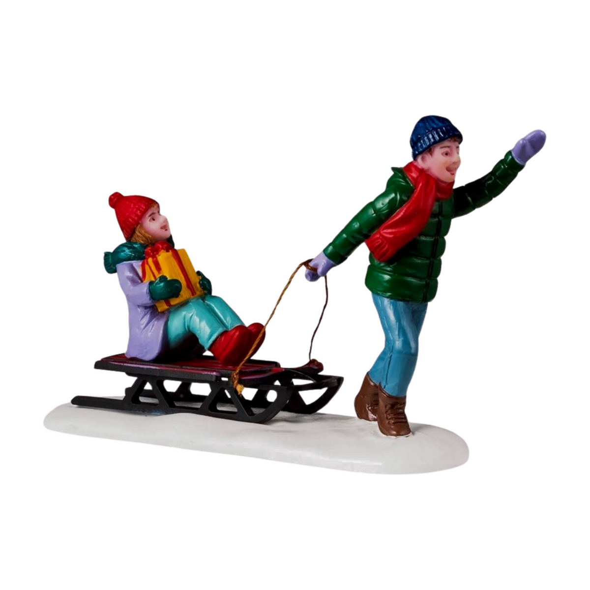 Christmas village figurine of a person pulling a child holding a gift on a sled, set on a snowy white base