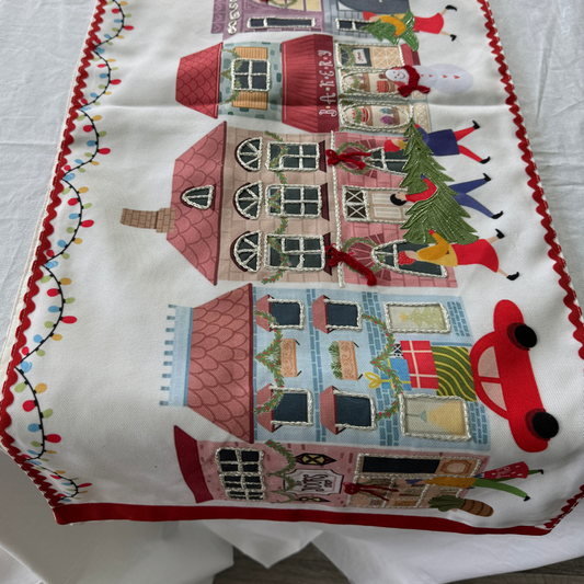 Fabric table runner with embroidered Christmas village scene and red scalloped trim