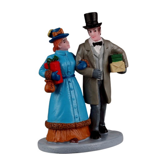 Christmas village figurine of a Victorian couple in period dress carrying wrapped gifts, the woman in blue, the man in a top hat 