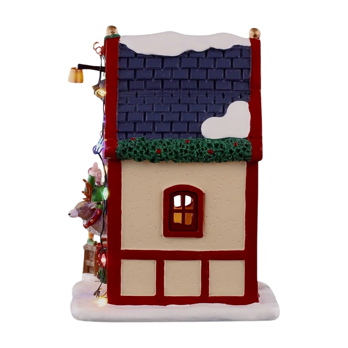 Left view of Comet's reindeer stable village building with blue-tiled roof, holly garland, lit window, and reindeer and elf figurines