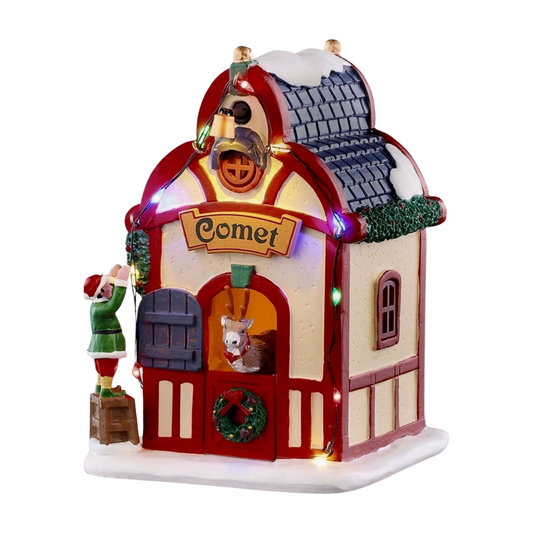 Front of Comet's reindeer stable village building with red domed roof, Comet sign, reindeer in doorway, and elf figurine on a crate