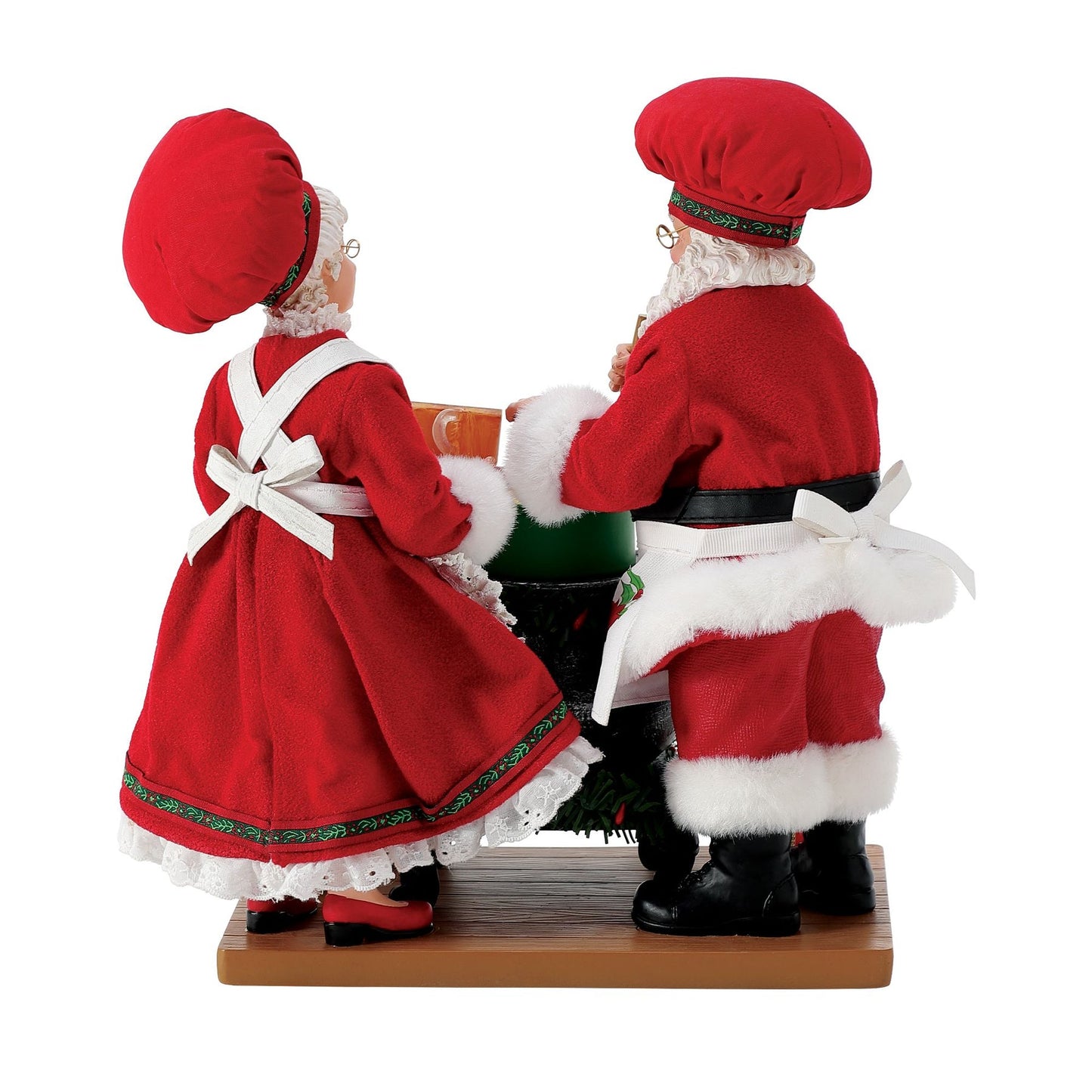 Rear view of Santa and Mrs. Claus figurines in matching red chef outfits and baker's hats, standing together at a decorated stove