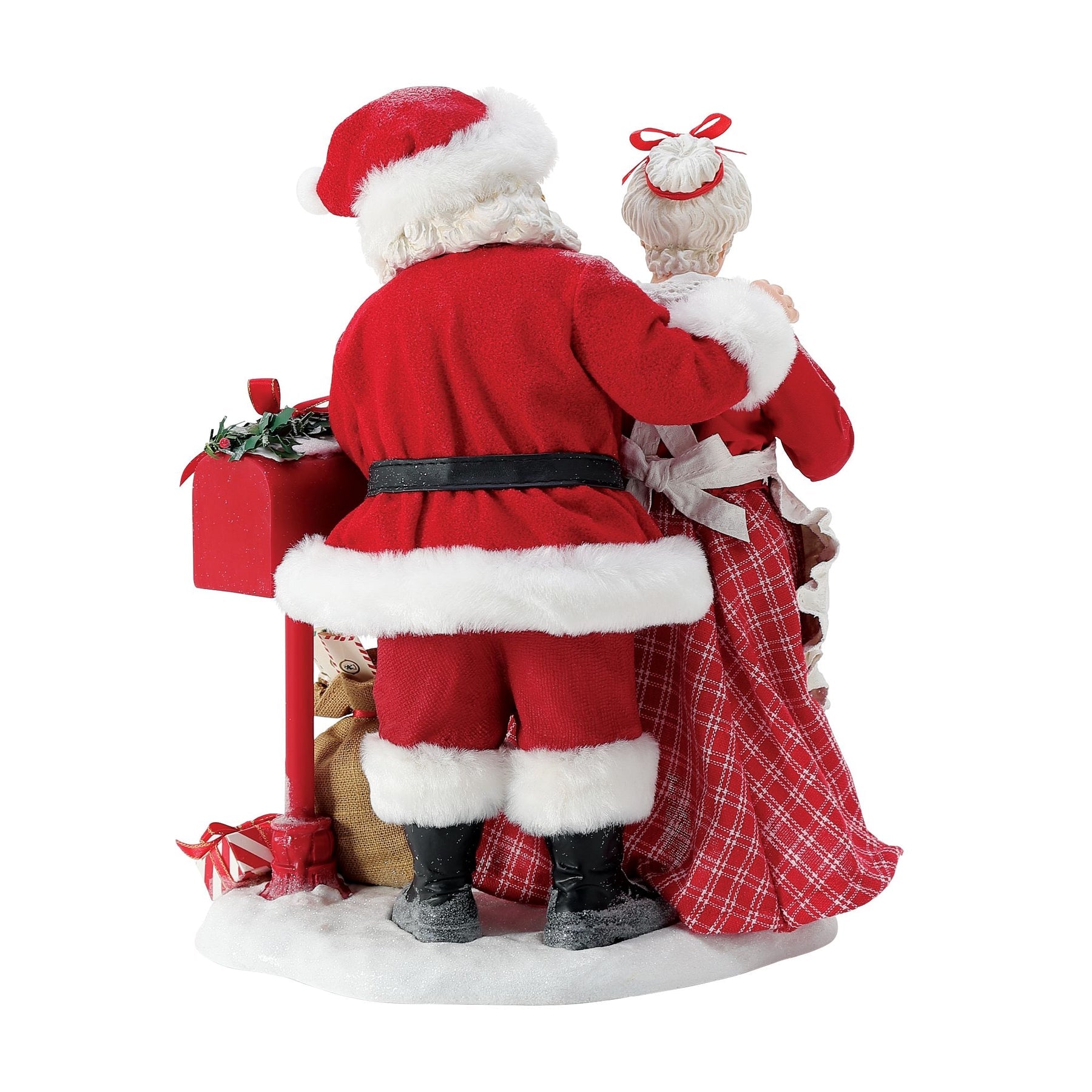 Rear view of Santa and Mrs. Claus figurines standing together at a red mailbox overflowing with holly, gifts and letters on a snowy base