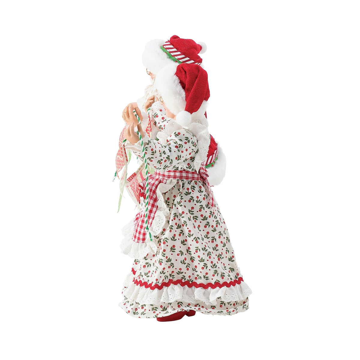 Side view of Mrs. Claus figurine in a holly-print dress with gingham sash, holding one end of a "Merry Christmas" pennant banner