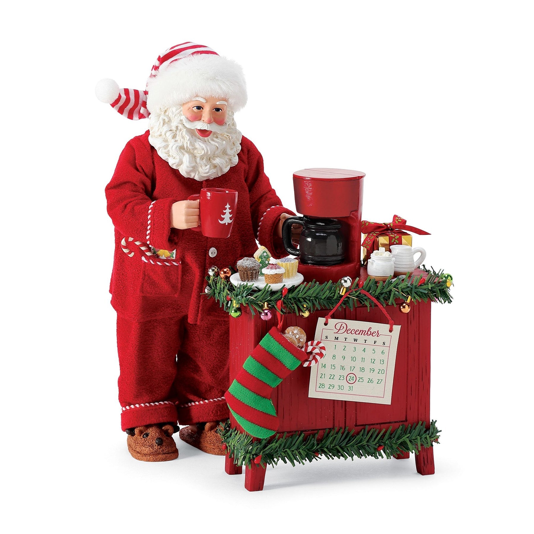 Santa figurine in red pyjamas with Christmas mug, coffee maker, cupcakes, stocking, and December 24 calendar on a decorated red sideboard
