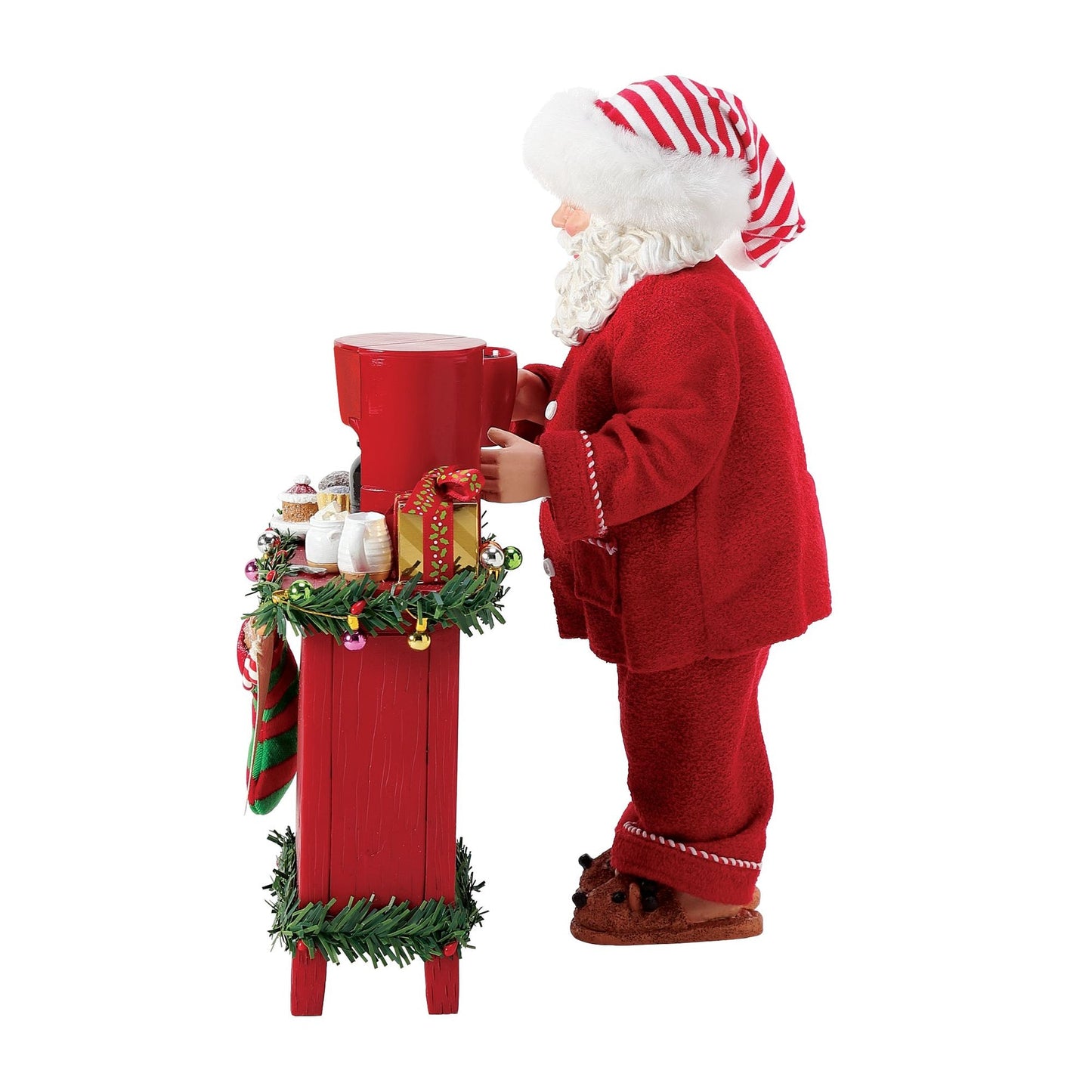Right-side view of Santa figurine in red pyjamas and striped hat, reaching toward a red coffee maker on a garland-trimmed sideboard 
