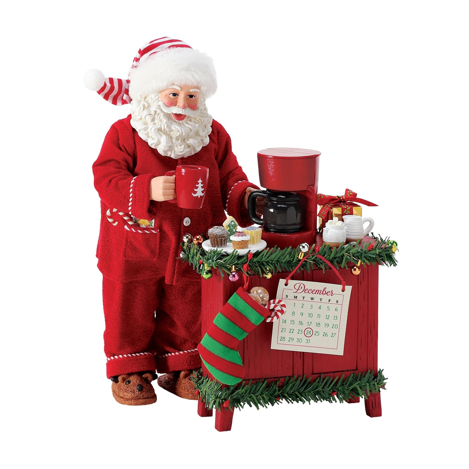 Santa figurine in red pyjamas holding a Christmas mug beside a sideboard with coffee maker, cupcakes, and a December 24 calendar