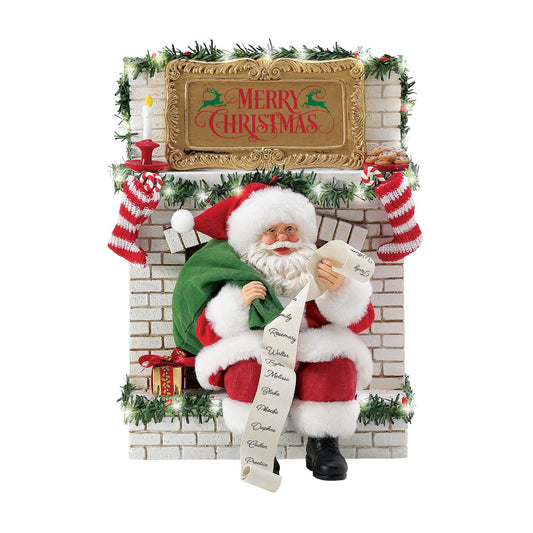 Santa figurine seated on a white brick fireplace with lit garland, reading a long naughty-or-nice list below a gold "Merry Christmas" mantel sign