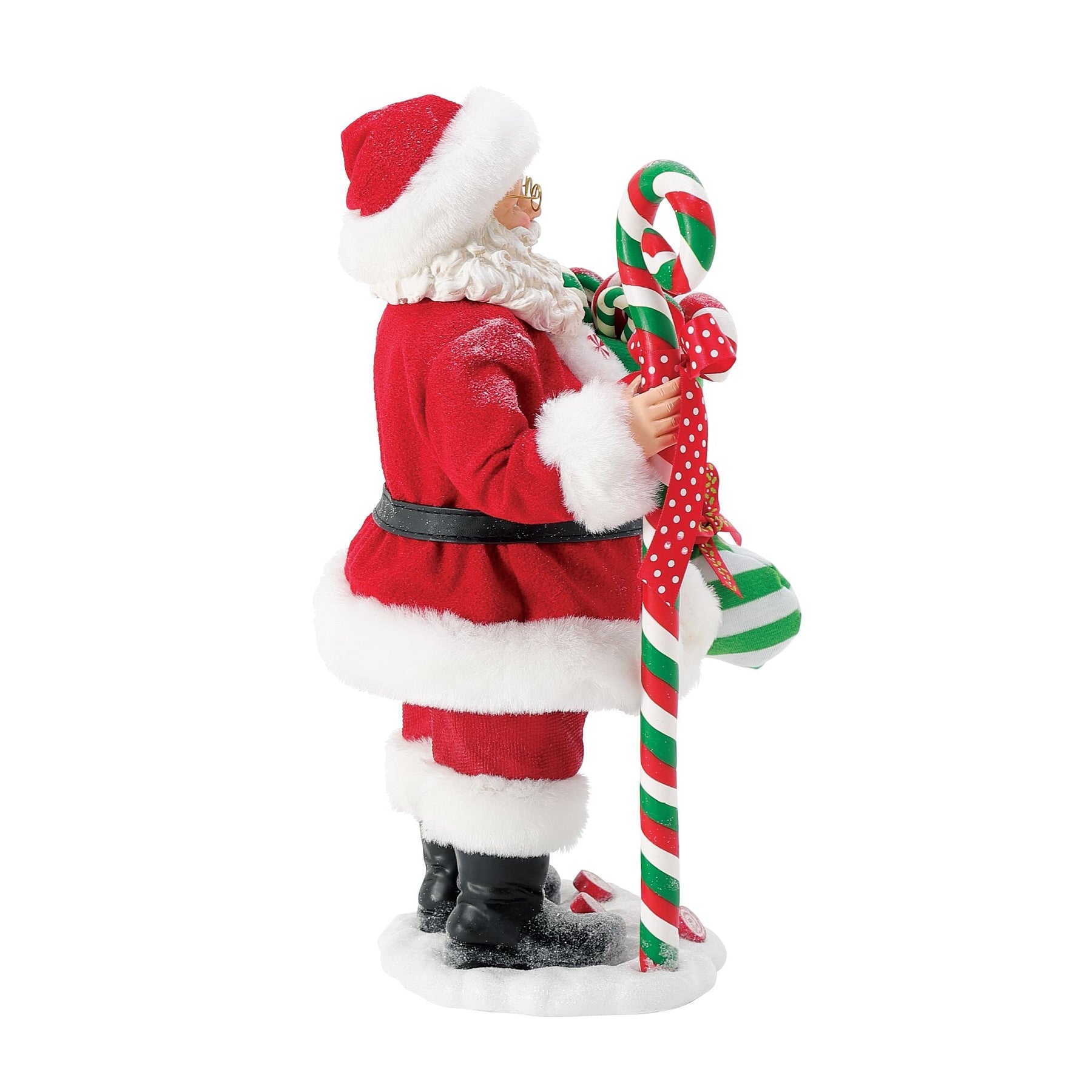 Three-quarter view of Santa figurine holding a striped green stocking overflowing with candy, standing beside a large striped candy cane