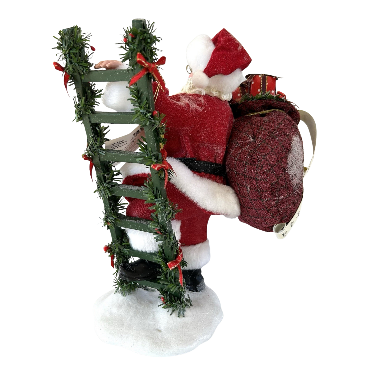 Rear view of a Santa figure climbing a garland-wrapped ladder with a large burgundy gift sack on his back, on a snow base