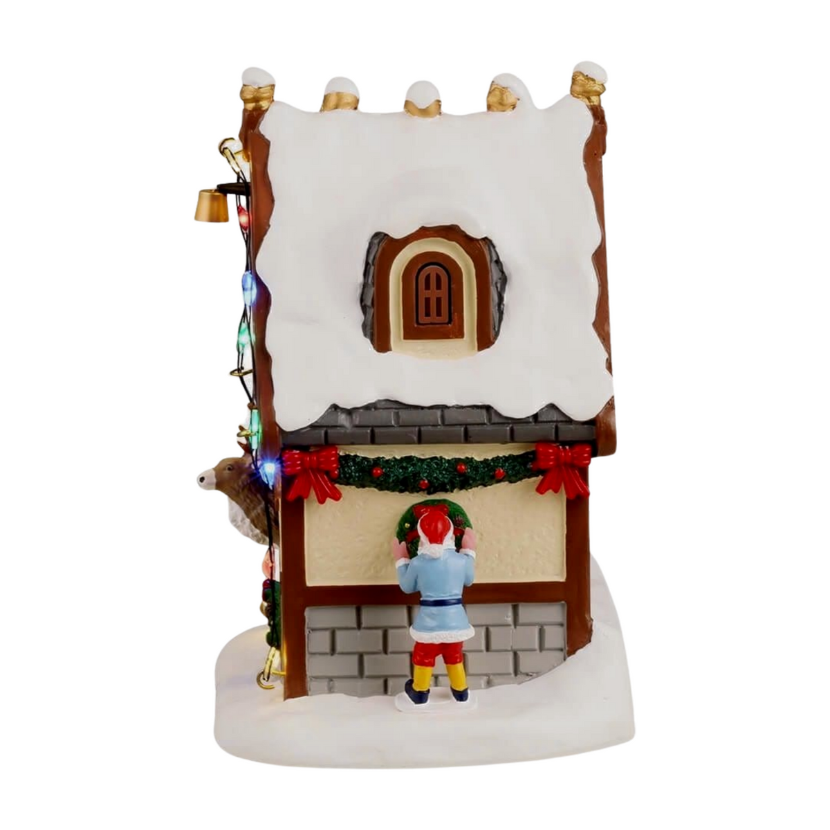  Left view of Donner's reindeer stable Christmas village building showing snow-covered roof, elf figure hanging a wreath, and coloured lights