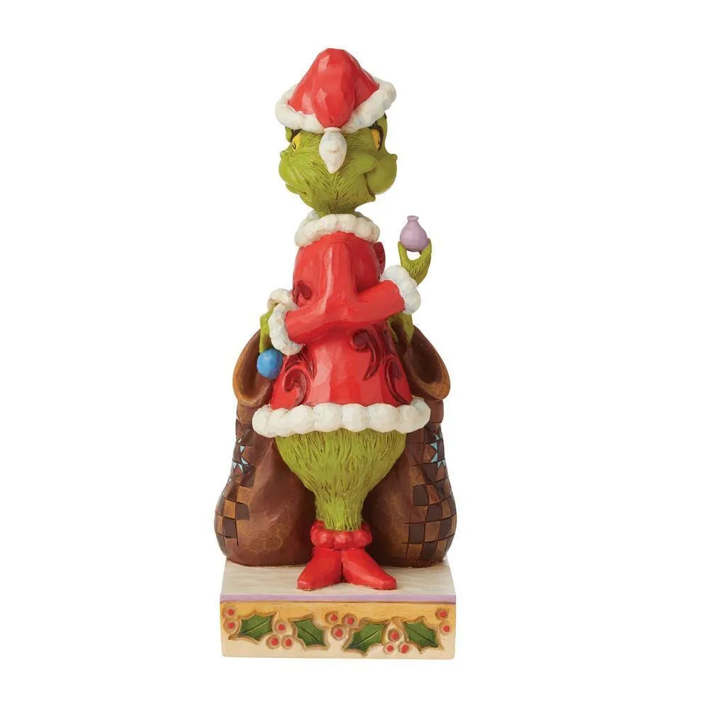 Side view of Grinch Naughty/Nice figurine in red scrollwork Santa suit, holding ornaments, patchwork sack, holly patterned base