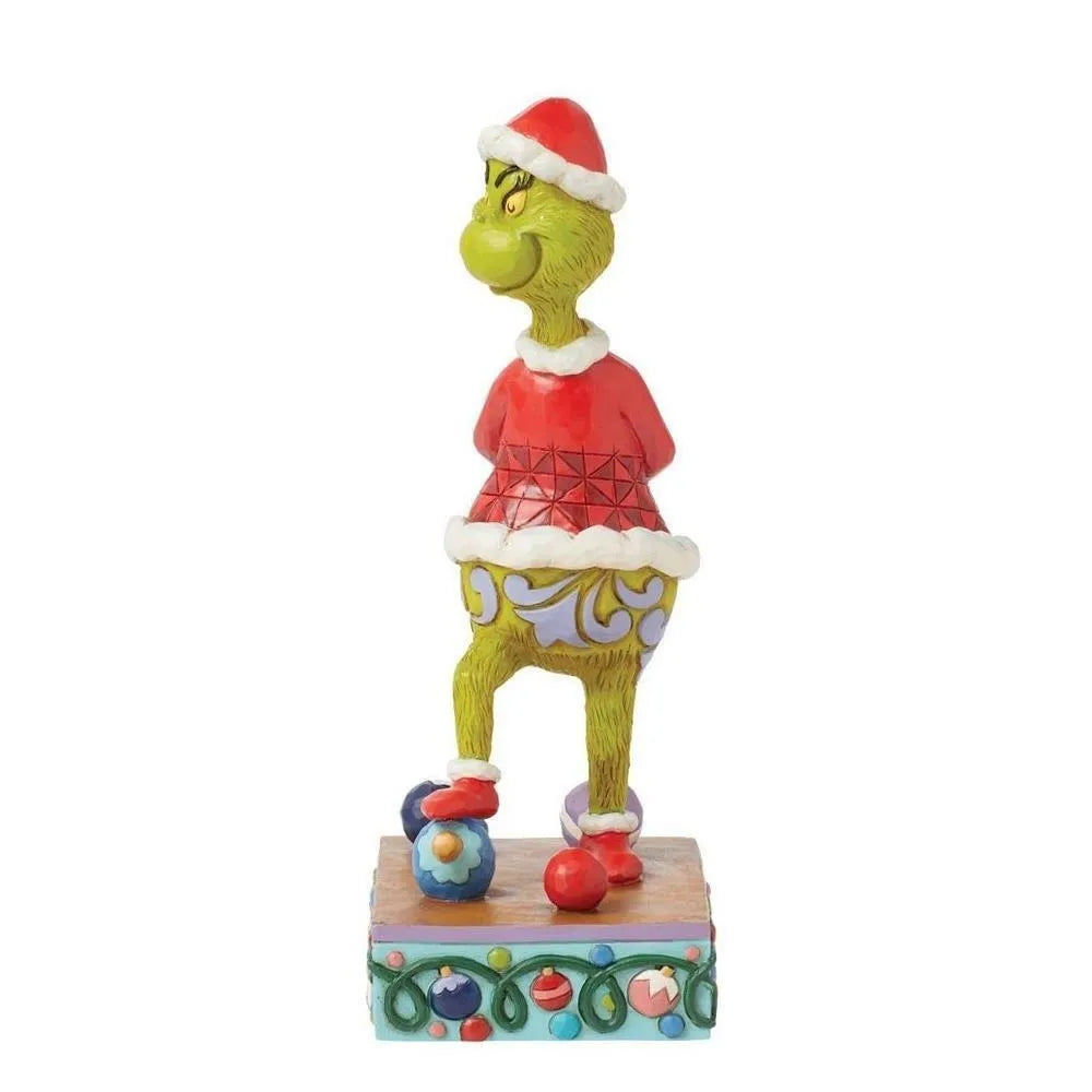 Opposite side view of a Grinch Santa figurine in a red jacket stepping over scattered baubles, on an ornament-garland base