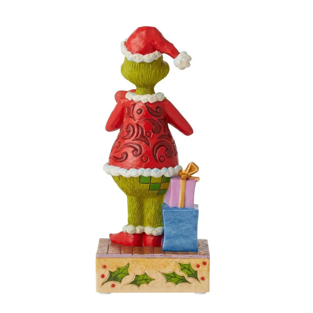 Rear view of Grinch figurine in red scrollwork coat and Santa hat, stacked gifts with gold bow beside holly-decorated base
