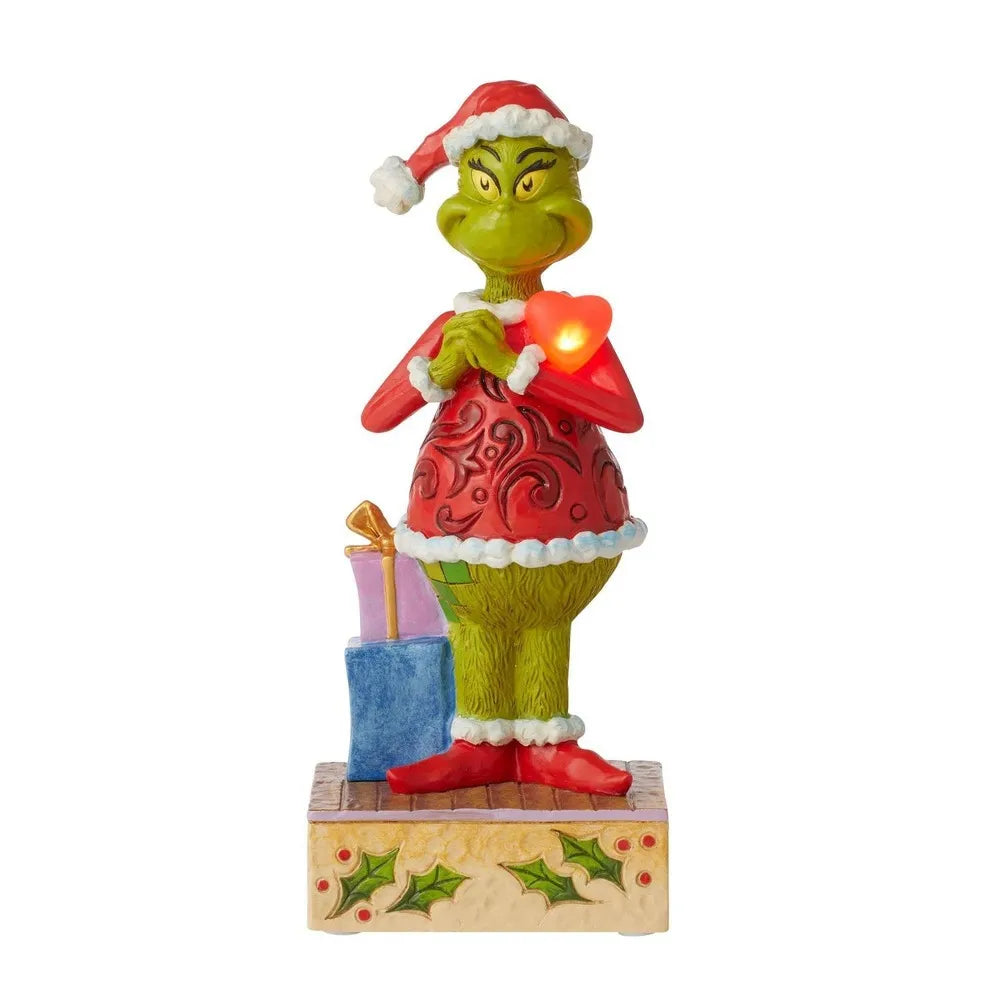 Grinch figurine holding an illuminated red heart, Santa hat and red scrollwork coat, stacked gifts, holly-decorated base 