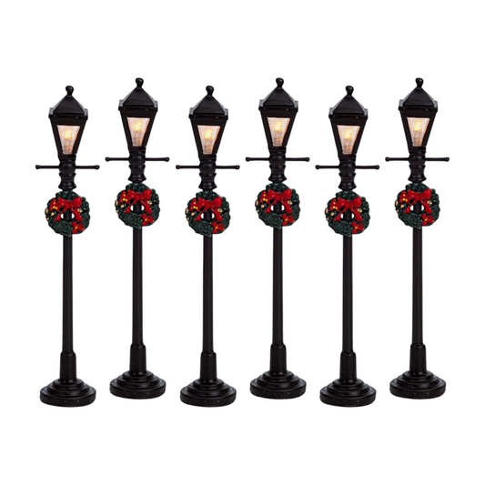 Set of six Christmas village gas lamp post figurines in black with warm lit lanterns and red-bow wreaths, on round bases