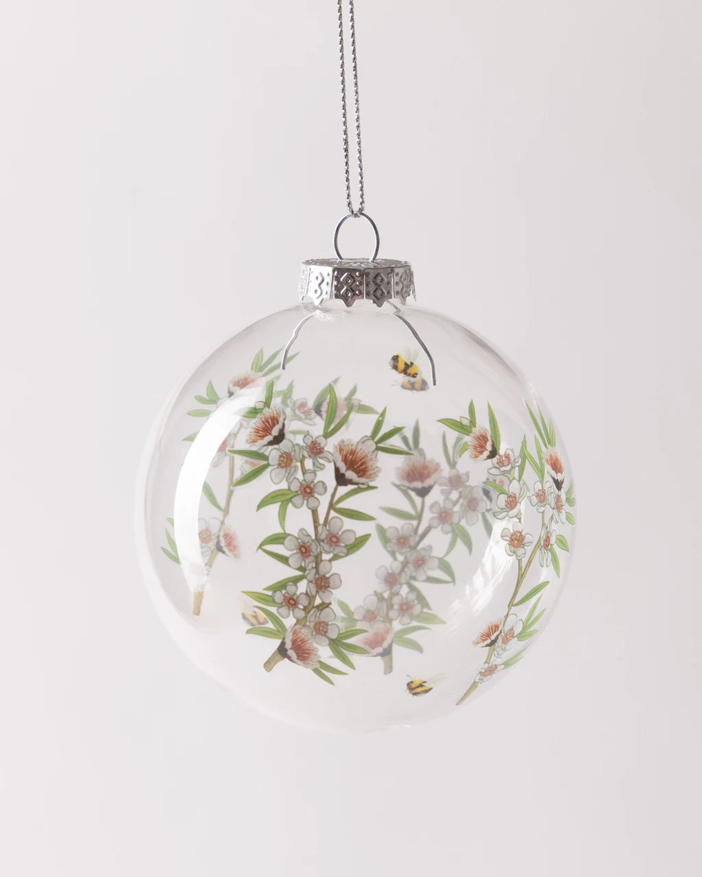 Clear glass bauble decorated with manuka flower and bee print design
