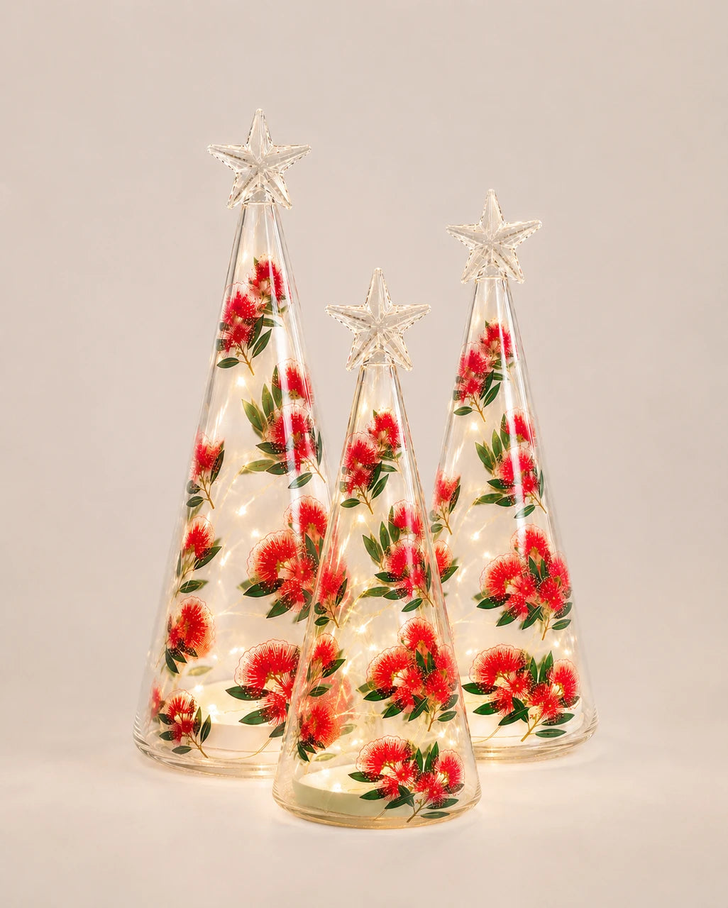 Three light-up glass cones with pohutukawa flower print in varying sizes, star toppers lit