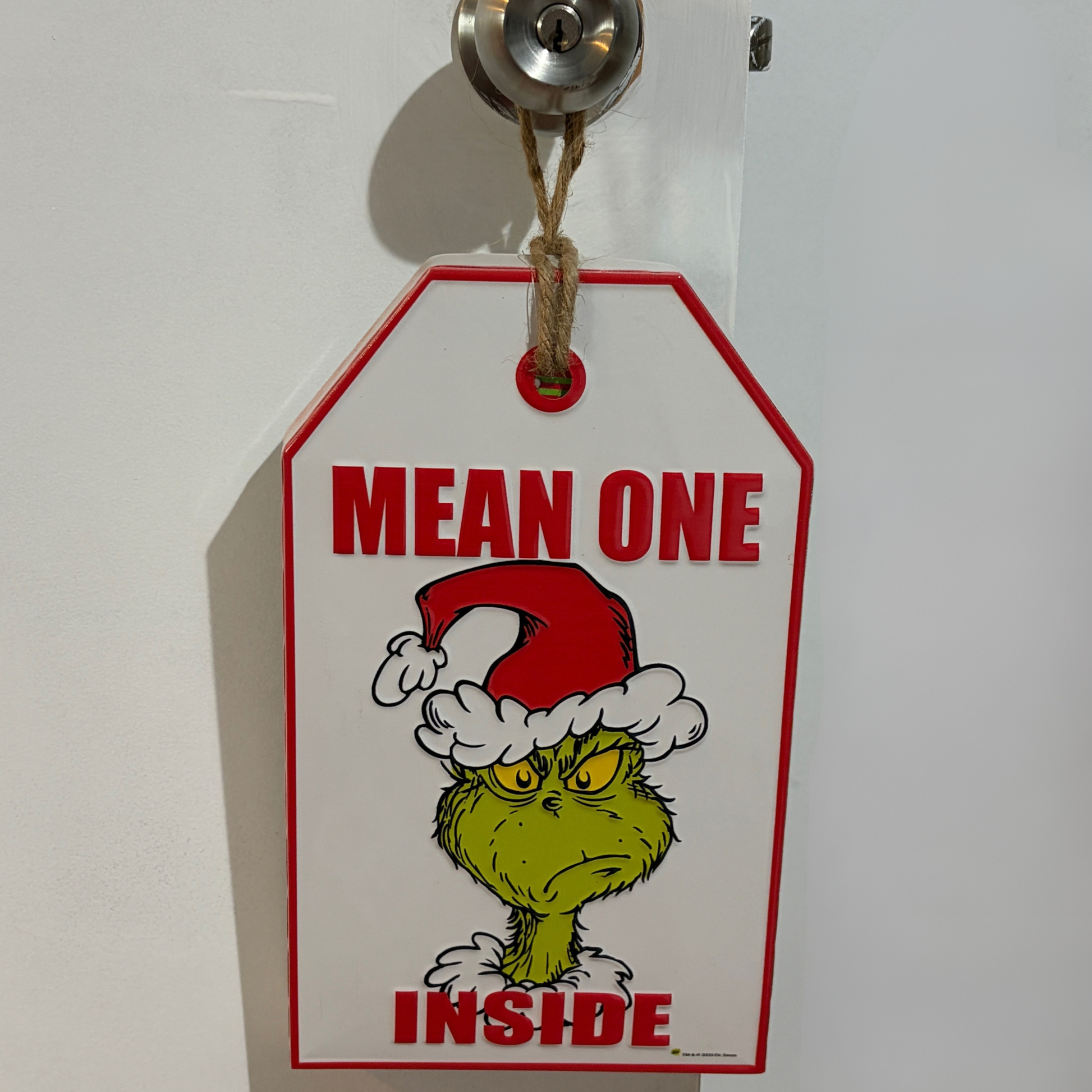 Door hanger featuring the Grinch wearing a Santa hat with red text reading “Mean One Inside”