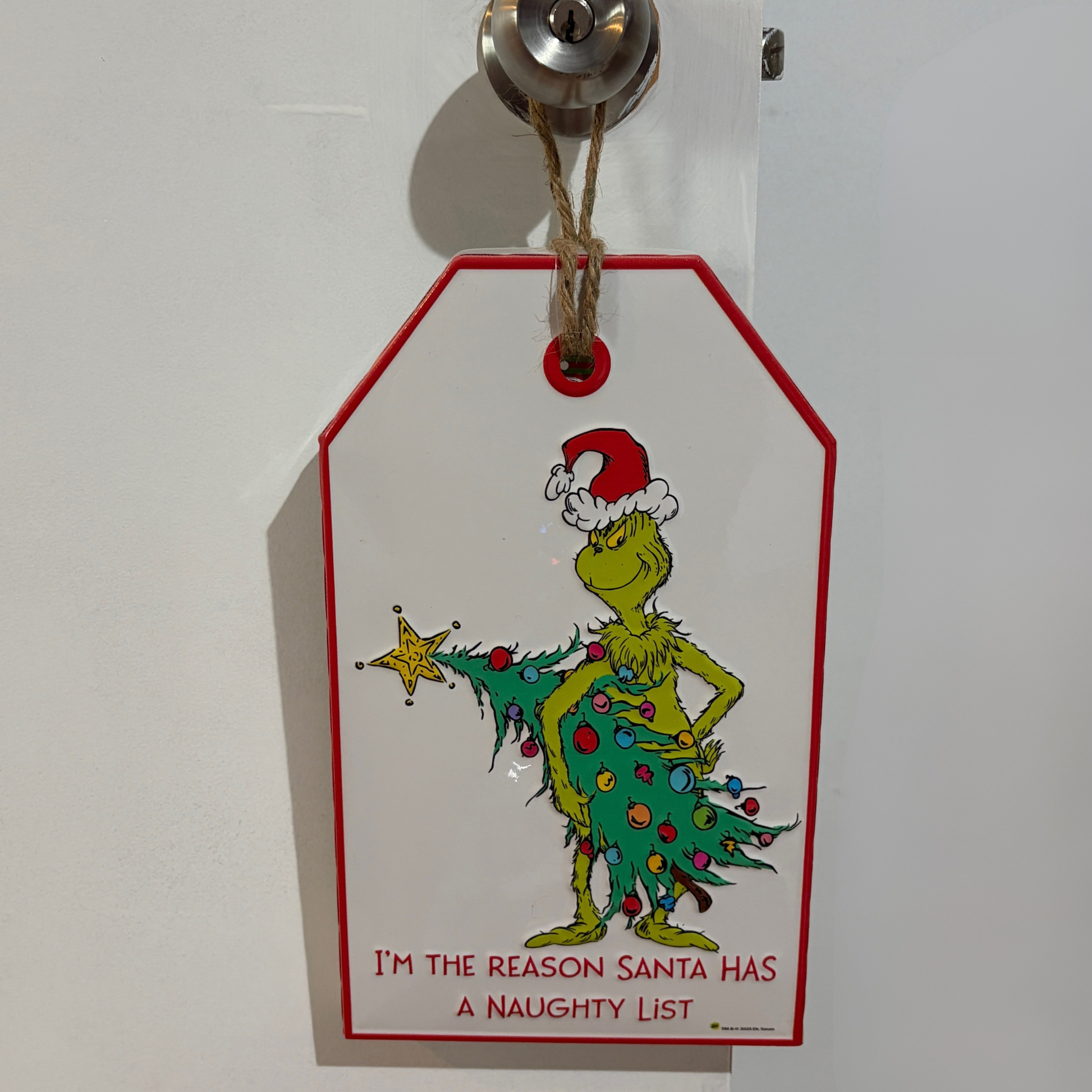 Door hanger featuring the Grinch in a Santa hat holding a Christmas tree with text reading “I’m the Reason Santa Has a Naughty List”
