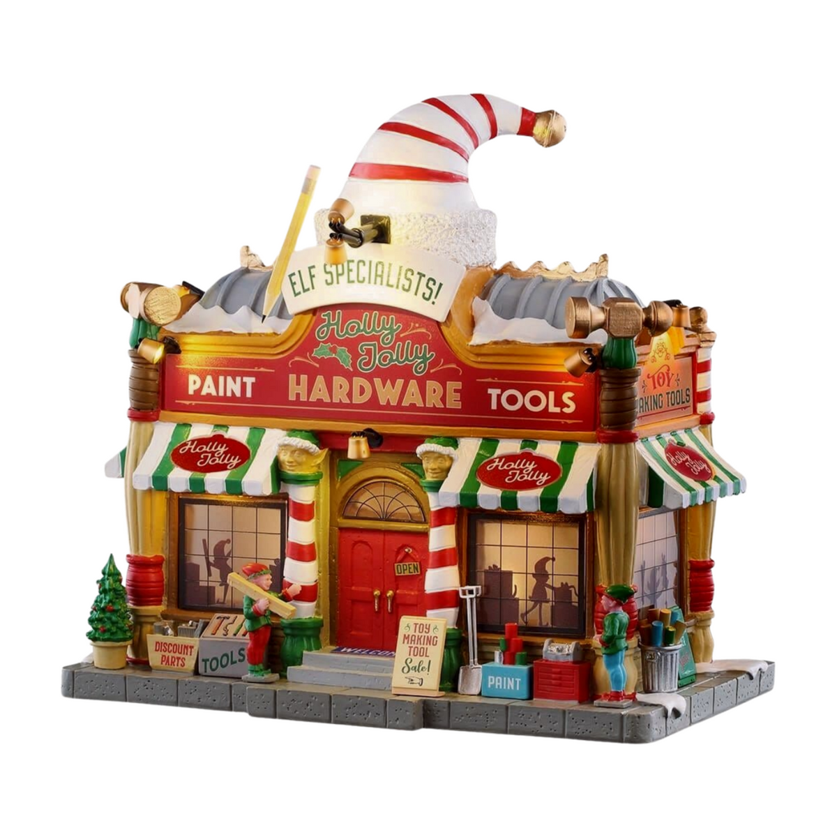  Illuminated Holly Jolly Hardware Christmas village building with oversized elf hat topper, striped awnings, elf figurines, paint and tools signage