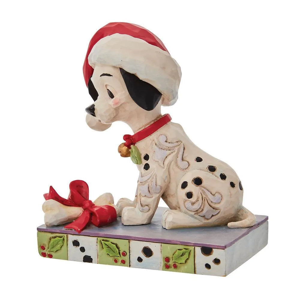 Three-quarter view of a Dalmatian puppy figurine in a Santa hat, red collar with bell, bone gift with red bow, holly-spot base