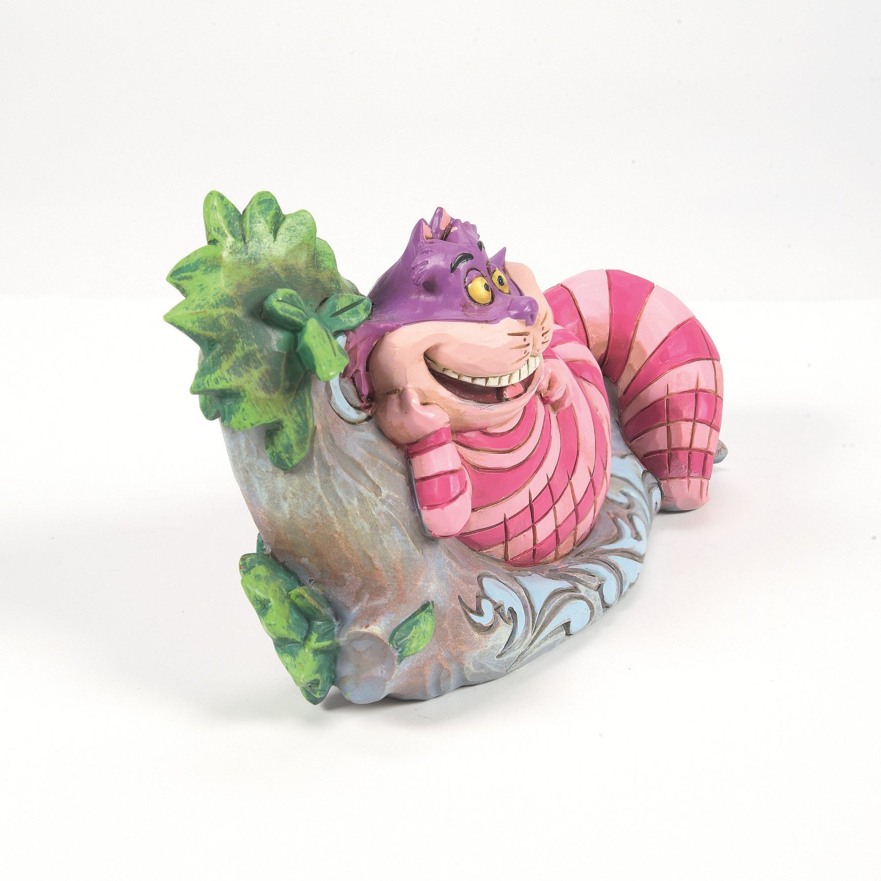 Cheshire Cat from Alice in Wonderland figurine left side view, lying on a painted log with green leaves and blue scrollwork detail