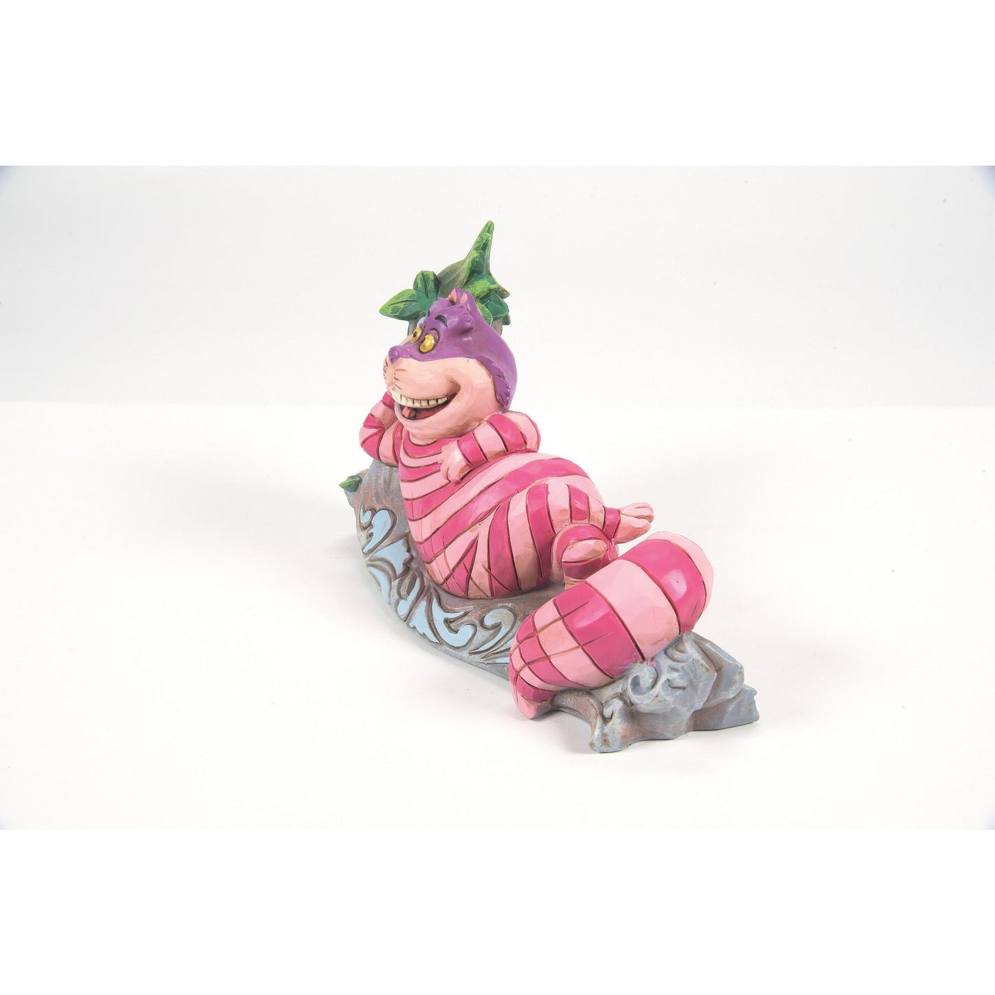 Cheshire Cat from Alice in Wonderland figurine right side view, lying on a painted log with green leaves and blue scrollwork detail