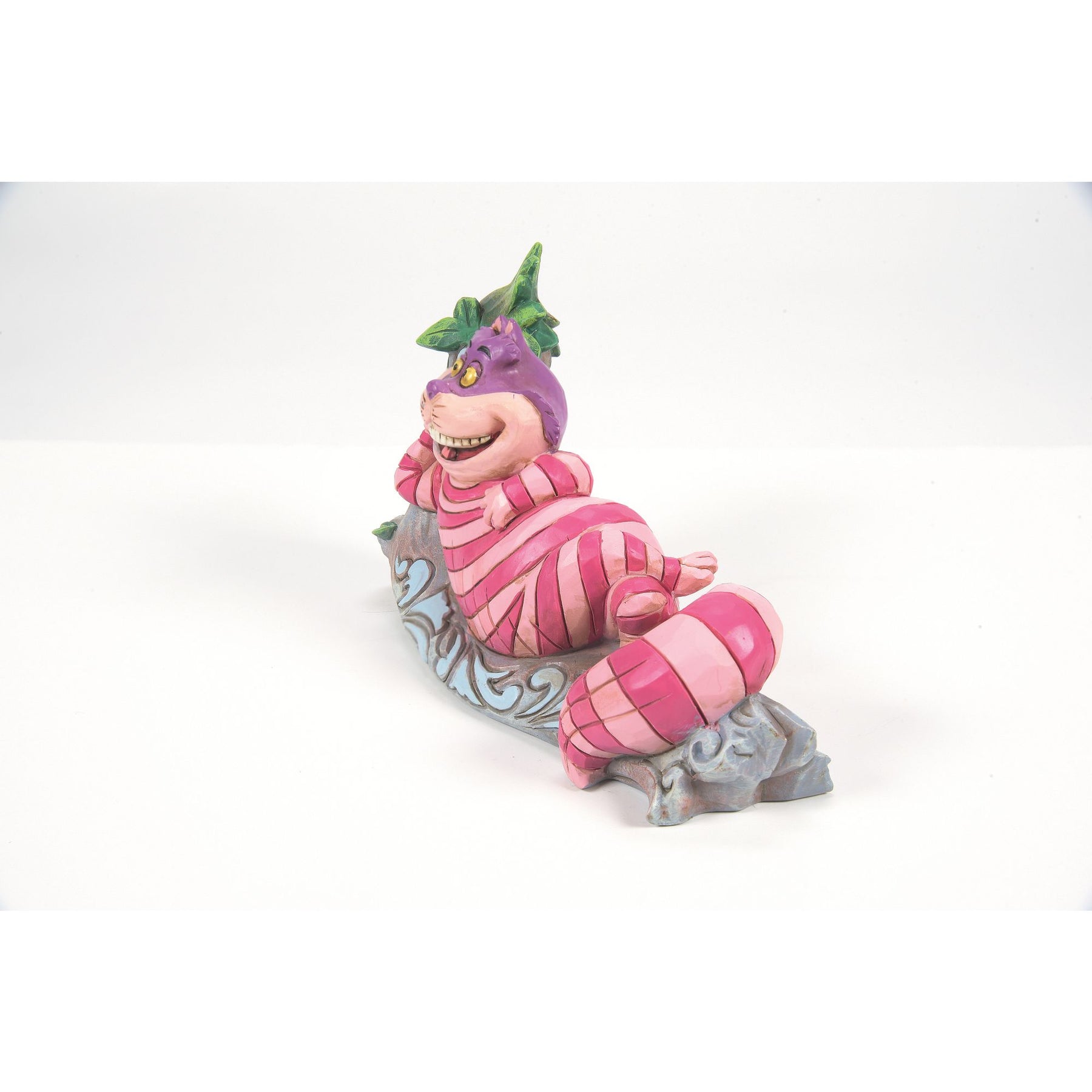 Cheshire Cat from Alice in Wonderland figurine right side view, lying on a painted log with green leaves and blue scrollwork detail
