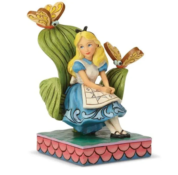 Alice in Wonderland figurine front view, seated between large green leaves with two butterfly creatures, blue scrollwork dress detail 