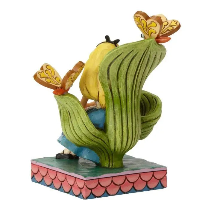 Alice in Wonderland figurine rear view showing large green leaf backdrop with two butterfly creatures on a pink scale painted base