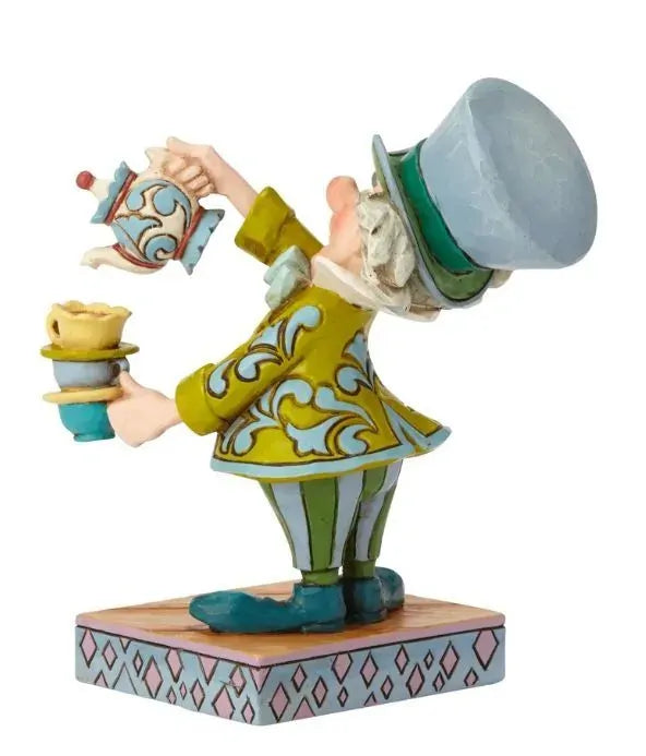 Mad Hatter from Alice in Wonderland figurine side view, pouring a teapot into stacked cups, yellow and teal scrollwork coat