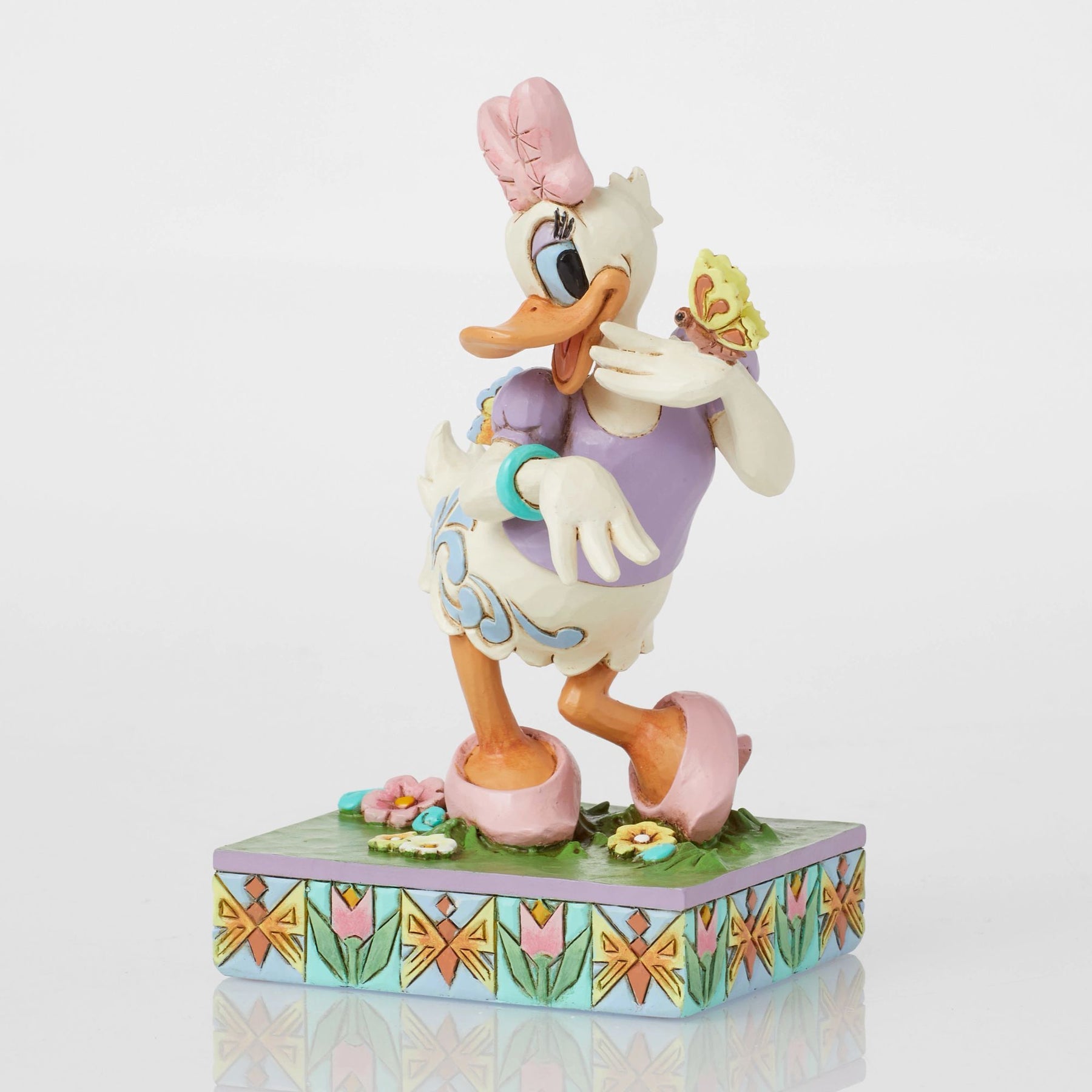 Angled front view of Daisy Duck spring figurine with butterfly, pink bow, purple top, scrollwork body, floral tulip base