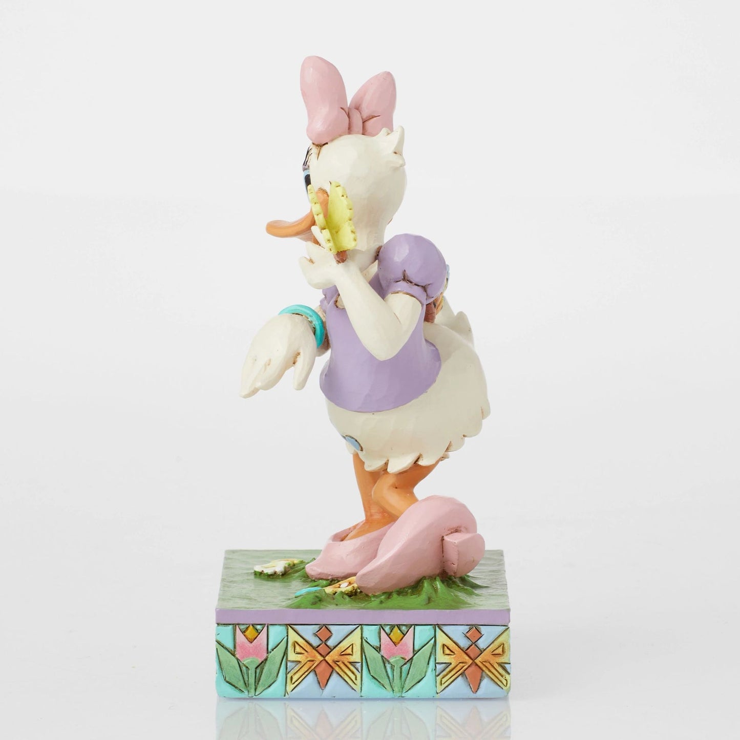 Side view of Daisy Duck spring figurine with two butterflies, pink bow, purple top, floral tulip painted base