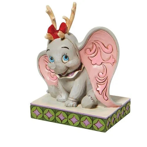 Angled front view of Dumbo Christmas figurine, reindeer antlers and red bow, seated with ears spread on a geometric base